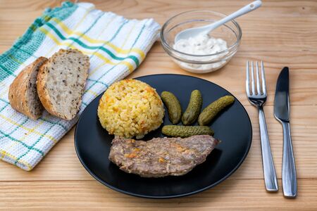 Prepared beef steak with rice risotto, pickles and sauce on black plate on wooden table backgroundの写真素材