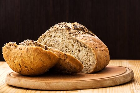 Loaf of wheat bread sprinkled with various seeds, with a cut slices of bread on a wooden tableの写真素材
