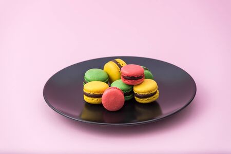 Tasty french macarons in a black plate on pink pastel background. Red, yellow and green macaronsの写真素材