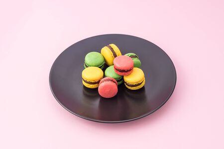 Tasty french macarons in a black plate on pink pastel background. Red, yellow and green macaronsの写真素材