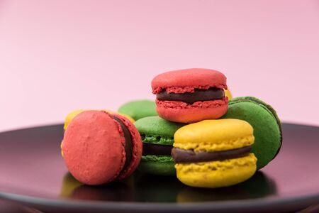 Close Up View of Tasty french macarons in a black plate on pink pastel background. Red, yellow and green macaronsの写真素材