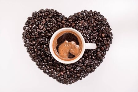 Top view of tasty coffee in cup or mug with heart made of coffee grains on white backgroundの写真素材