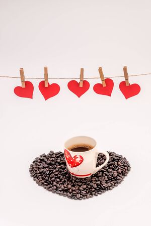 Cup of Coffee with heart made of coffee grains on white background and Clothes pegs and red paper hearts on rope above. Valentines day conceptの写真素材