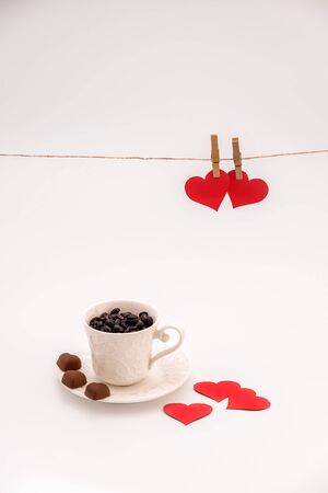 Cup of Coffee with heart shaped chocolate cookies on white background and Clothes pegs and red paper hearts on rope above. Valentines day conceptの写真素材