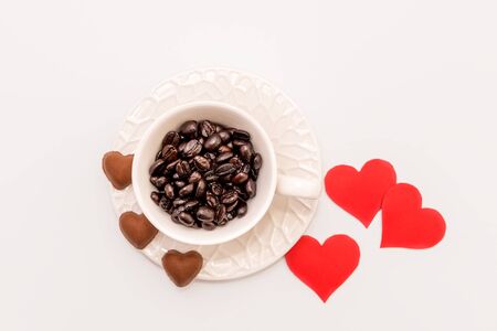 Top View of Cup of Coffee grains with heart shaped chocolate cookies and red paper hearts on white background. Valentines day conceptの写真素材