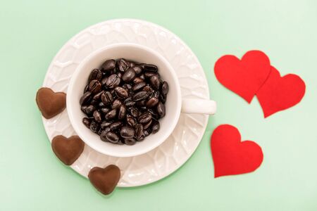 Top View of Cup of Coffee grains with heart shaped chocolate cookies and red paper hearts on lime green background. Valentines day conceptの写真素材