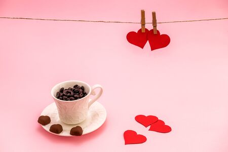 Cup of Coffee grains with heart shaped chocolate cookies and red paper hearts on pink pastel background. Valentines day conceptの写真素材