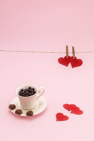 Cup of Coffee grains with heart shaped chocolate cookies and red paper hearts on pink pastel background. Valentines day conceptの写真素材