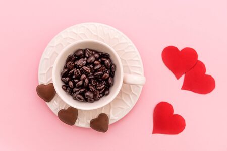 Top View of Cup of Coffee grains with heart shaped chocolate cookies and red paper hearts on pink pastel background. Valentines day conceptの写真素材
