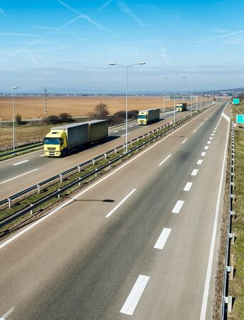 Caravan or convoy of Yellow lorry trucks on country highway under a dramatic skyの写真素材