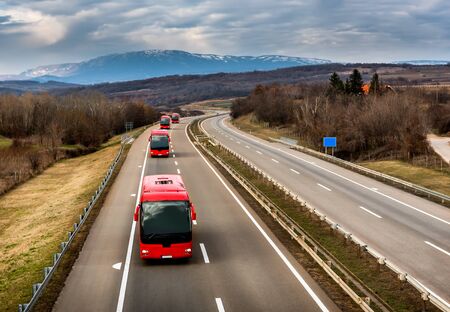 Caravan or convoy of Red buses in line traveling on a highway country highwayの写真素材