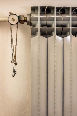 Close up heating radiator with Radiator Keys Brass Air Vent Clock Type hanging on a rope. Central heating concept, radiator heaterの写真素材
