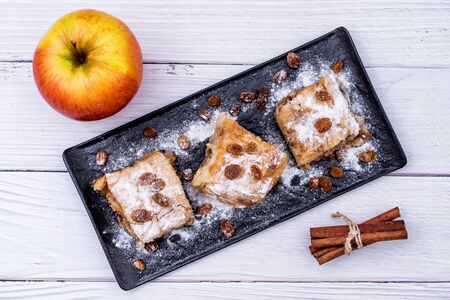 Slices of homemade Apple pie strudel in a plate with ingredients on a rustic white wooden table. Pie with apples, raisins and cinnamon, sweet pastries - Top Viewの写真素材