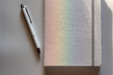 White Employee Handbook or manual with White pen on white surface lit by a light dispersed into rainbow - personnel management policy, explains business goals, results, defines personnel practicesの写真素材