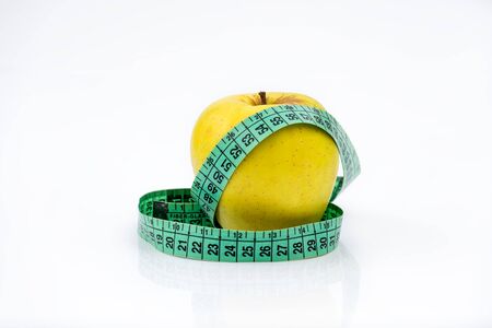 Golden Yellow apple and a green measuring tape on white background - all about proper nutrition and metabolism.の写真素材