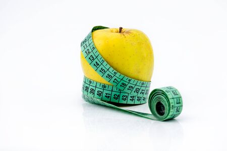 Golden Yellow apple and a green measuring tape on white background - all about proper nutrition and metabolism.の写真素材