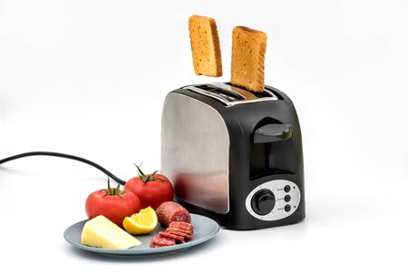 Toasts jumping out of retro style black and metallic toaster on white background. Levitation food. Kitchen equipment for fresh morning meal with sandwich ingredients - tomato, cheese, dried sausage.の写真素材