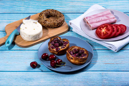 Breakfast served at blue wooden table with juice, ham, pecorino cheese, tomato, corn bread pretzel and sweet cherry pie. Continental delicious healthy breakfast tableの写真素材