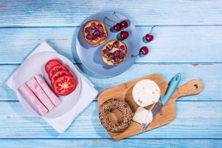 Breakfast served at blue wooden table with juice, ham, pecorino cheese, tomato, corn bread pretzel and sweet cherry pie. Continental delicious healthy breakfast tableの写真素材