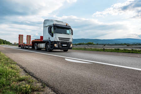 Semi trailer transportation truck with empty trailer on a highway driving at bright sunny sunset. Transportation vehicleの写真素材