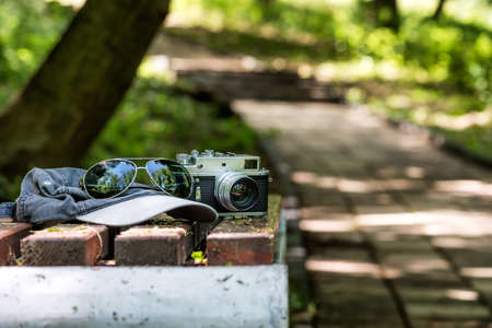 Vintage Phototographer Accesories on a bench un the park. Rangefinder old camera, sunglasses and a...