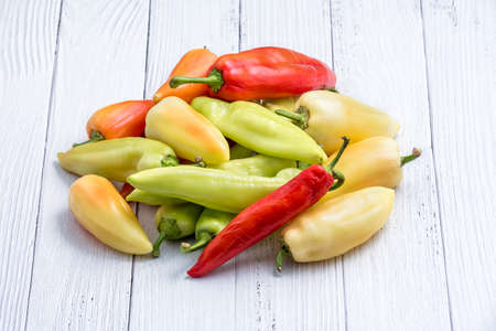 Pile of fresh ripe chili peppers for sale in vegetables market as background. Various red and green peppers on white wooden tableの写真素材