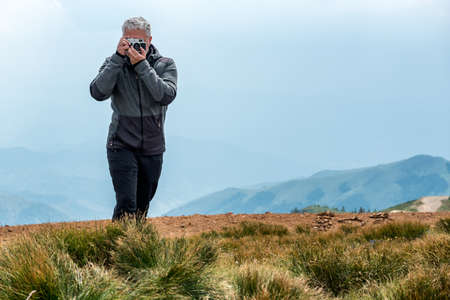 Photographer with old analog camera at a Mountain top. Mountain landscape view. Mountain layers landscape. Meadows and mountains landscape. Blue mountains layers landscape. Top of the Mountainsの写真素材