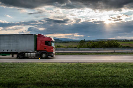 Red truck is on highway - business, commercial, cargo transportation concept, beautiful sunset sky, clear and blank space - side viewの写真素材