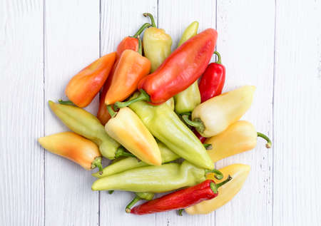 Pile of fresh ripe chili peppers for sale in vegetables market as background. Various red and green peppers on white wooden tableの写真素材