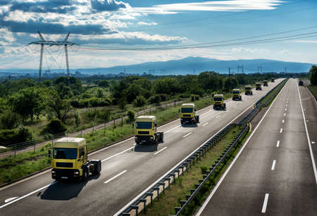 Convoy of many yellow transportation semi trucks in line as a caravan or convoy on a countryside highway under a blue skyの写真素材