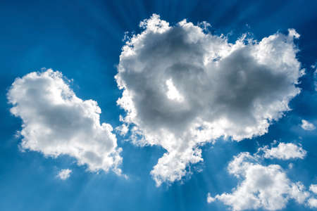 White cumulus clouds and a blue sky with sun raysの写真素材