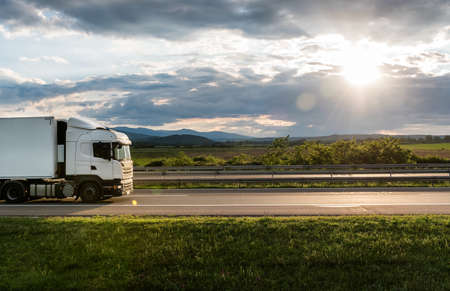 White truck is on highway - business, commercial, cargo transportation concept, beautiful sunset sky, clear and blank space - side viewの写真素材