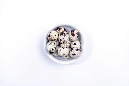 Quail eggs in white ceramic bowl isolated on white background. Top view. Detailed closeup of spotted quail eggsの写真素材