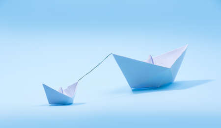 Paper boats - Tugboat or Remorker pulling a big boat on blue background. Little helper concept, Tugboatの写真素材