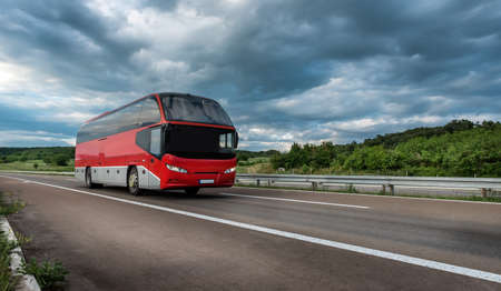 Generic Red Modern comfortable tourist bus driving through highway on a cloudy day. Travel and coach tourism concept. Trip and journey by vehicleの写真素材