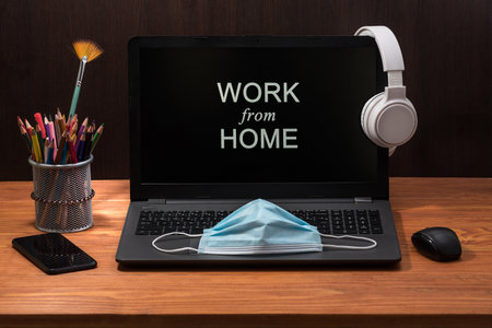 Work from home during Coronavirus pandemic quarantine isolation. Working remotely home concept. Comfortable working place in home office with laptop on the table with Surgical Mask, Headphones, and ofの写真素材