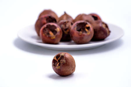 Fresh ripe organic common medlar fruit  on white background with more medlars on a plate in the background with soft focus. Healthy food Mespilus germanicaの写真素材