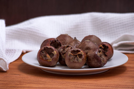 Fresh ripe organic common medlar fruit on a plate on wooden rustic background. Healthy food Mespilus germanicaの写真素材