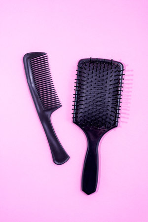 Black hair brush with handle and Black Comb on a textured pink background. Combing and hair care, 

hairdressing tools, haberdashery. Studio shot. Copy space. Top view.の写真素材
