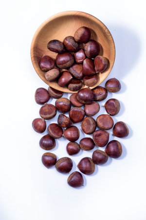 Chestnuts spilled from wooden bowl on white background. Castanea sativa, sweet ripe Chestnutsの写真素材