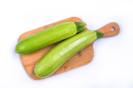 Courgette or Zucchini on wooden cutting board - green spotted vegetable for cooking vegetarian and healthy food, agricultural product isolated on white backgroundの写真素材