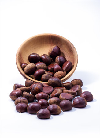 Chestnuts spilled from wooden bowl on white background. Castanea sativa, sweet ripe Chestnutsの写真素材