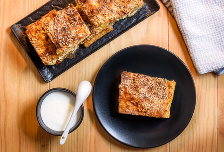 Slice of Homemade spinach pie with cottage cheese on a plate served with yogurt or creme fraiche on a wooden table. Selective focus. Top Viewの写真素材