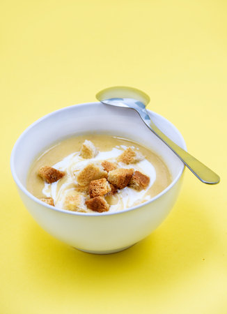 Creamy chicken and zucchini thick soup served with integral bread croutons in whitek bowl on yellow background. Selective focus. Copy space. Top Viewの写真素材