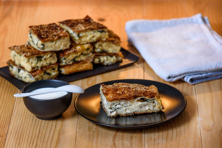Slice of Homemade spinach pie with cottage cheese on a plate served with yogurt or creme fraiche on a wooden table. Selective focusの写真素材