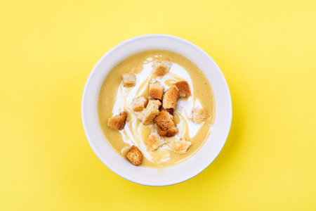 Creamy chicken and zucchini thick soup served with integral bread croutons in whitek bowl on yellow background. Selective focus. Copy space. Top Viewの写真素材