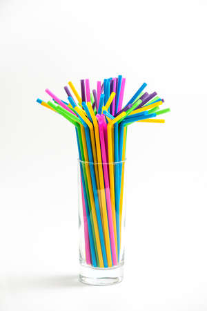 Multicolored plastic cocktail straws in a glass tumble on white backgroundの写真素材