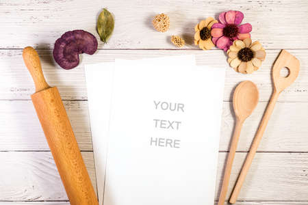 A paper copy space mockup photograph styled in a kitchen or bakery setting, with a rolling pin and wooden spoons on a wooden surfaceの写真素材