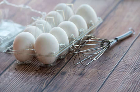 Fresh white eggs with stainless steel whisk on a wooden table. Close uo shot with shallow dofの写真素材