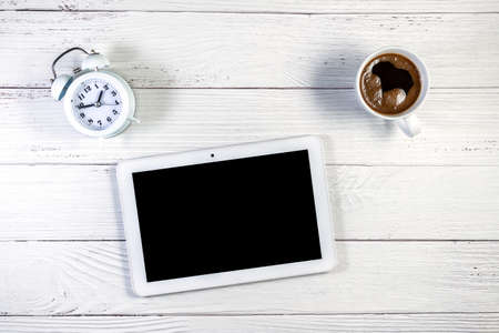 Tablet mockup with clipping path, on a white wooden table with coffee mug and white alarm clockの写真素材